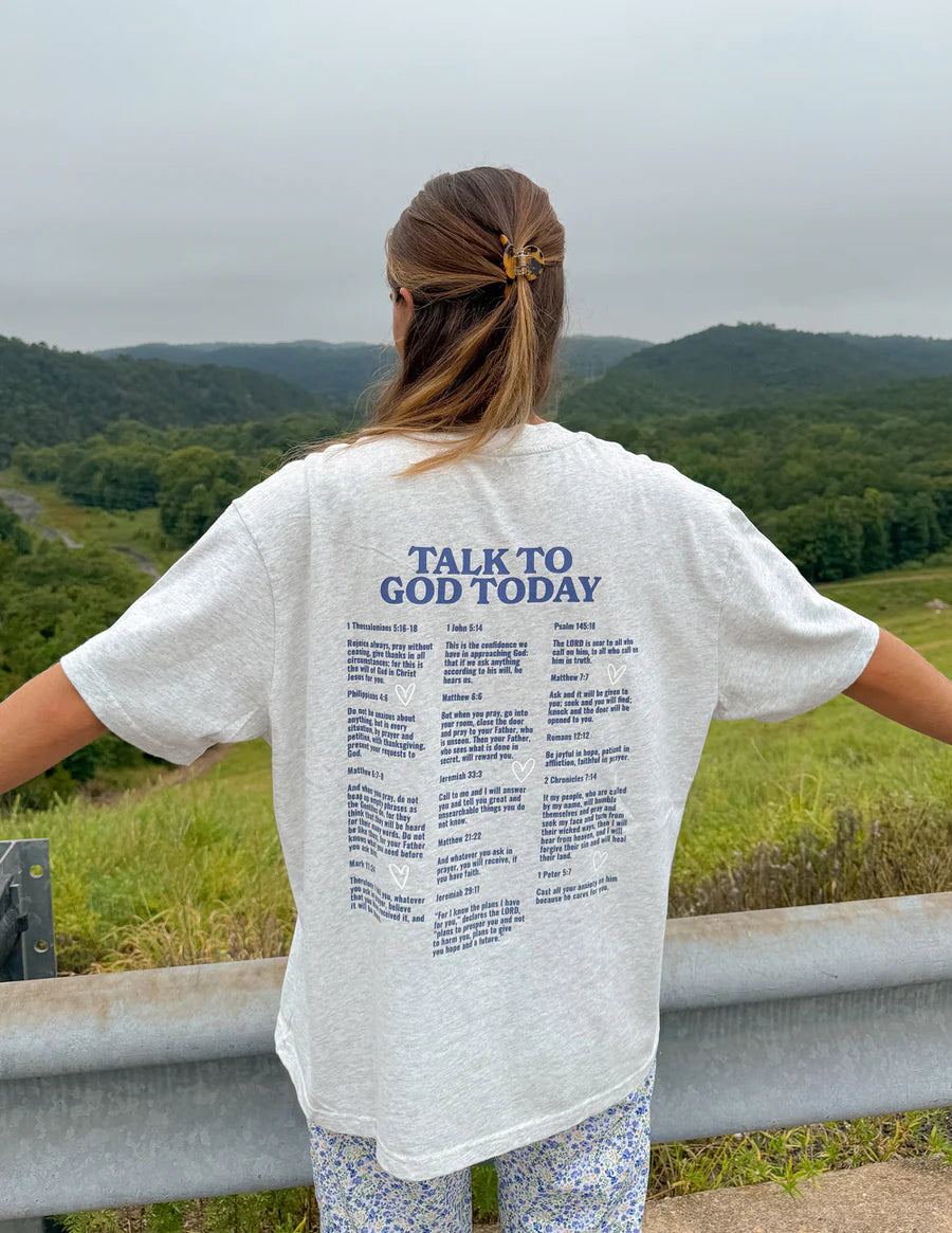 Person wearing a white t-shirt with 'Talk to God Today' text, standing on a scenic overlook.